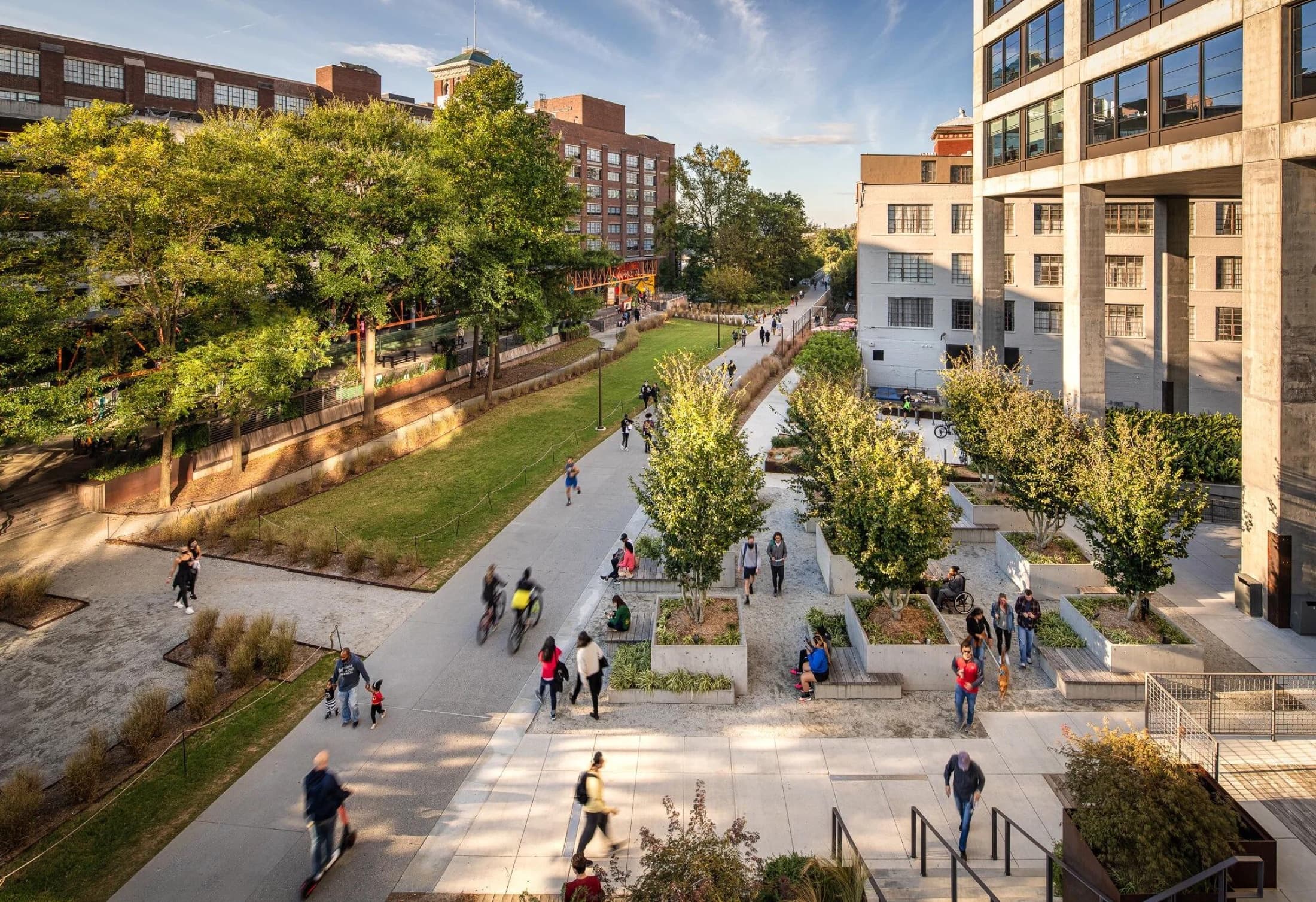 A public path between converted industrial buildings filled with people walking, cycling, and gathering